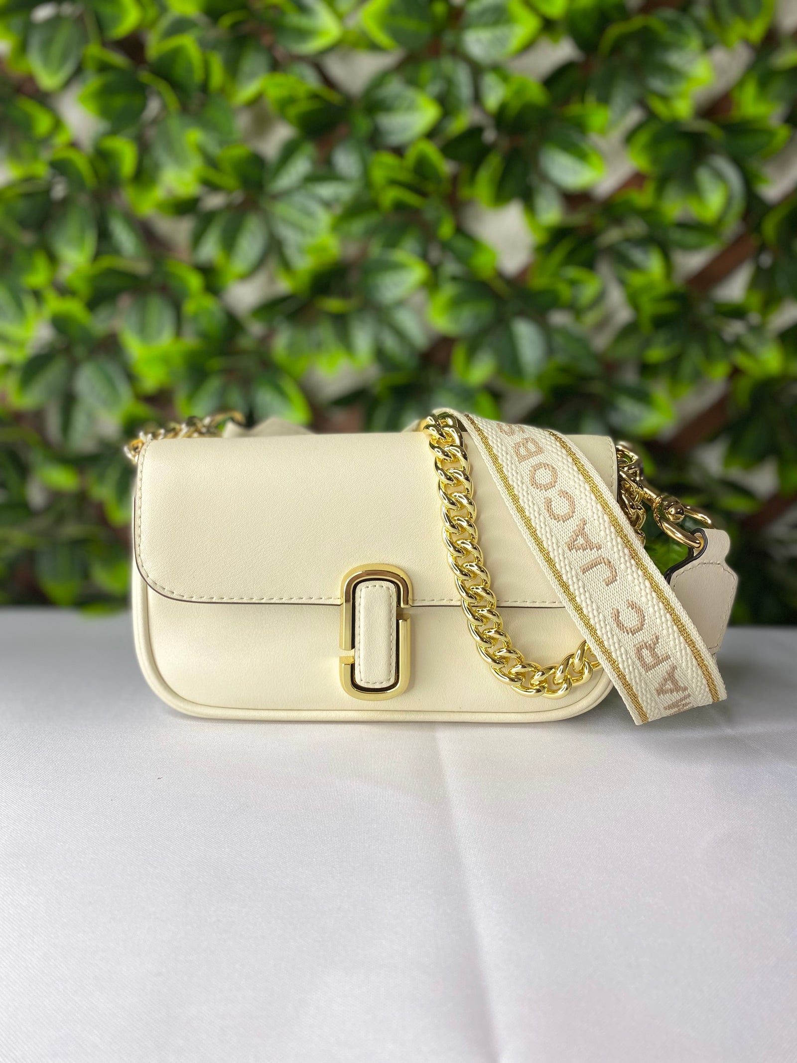 Crossbody Marc Jacobs Cloud White mini en piel suave, con correa de cadena y detalles metálicos J Marc.